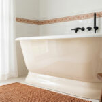 Baignoire îlot crème dans une salle de bain lumineuse avec carrelage blanc et accents terracotta.