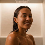 Une jeune femme souriante prend une douche relaxante, profitant d'une eau douce pour sa peau et ses cheveux.