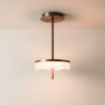 Une lampe suspendue moderne avec une structure en métal cuivré et un diffuseur en verre ondulé allumée sur fond blanc.