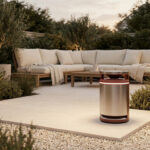Piège à moustiques cylindrique en métal posé sur une terrasse moderne avec salon de jardin en arrière-plan.